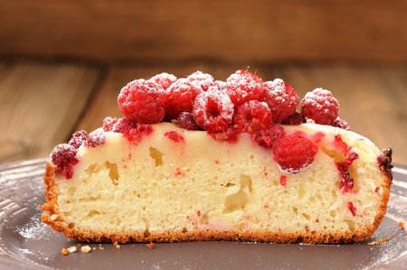 Homemade sponge cake with fresh juicy wild raspberries and icing sugar cut in halves in brown plate...