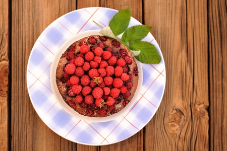 Homemade round chocolate cake with fresh wild raspberries and green leaves in blue checkered plate on wooden table copyspace topview top viewの写真素材