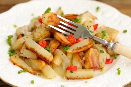 Fried potatoes with scallion and chili in white plate with fork closeup macro