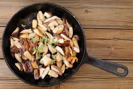 Fried porcini mushrooms with fresh thyme in cast iron skillet on wooden background copyspace top view horizontalの写真素材