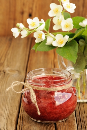 Homemade strawberry jam in glass jar and bunch of jasmine verticalの写真素材