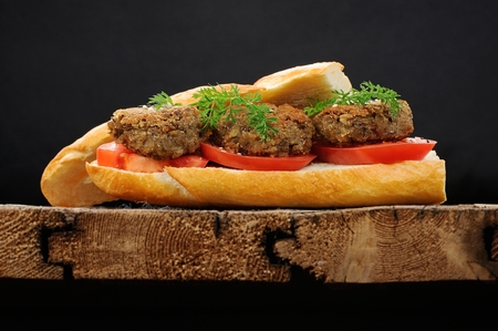Lentil patty sandwich with tomato and carrot greens in old wooden board horizontalの写真素材
