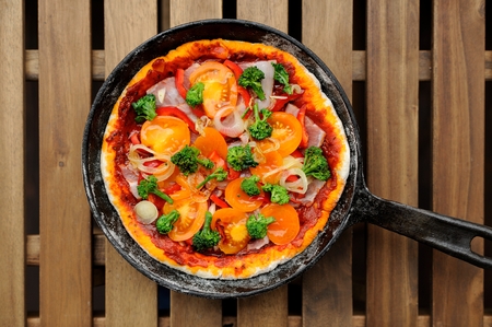 Raw round pizza with yellow cherry tomatoes, onion, garlic and broccoli in cast iron skillet horizontalの写真素材