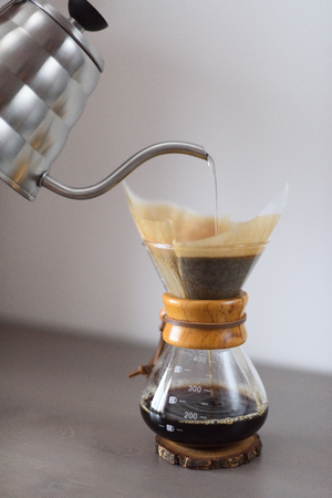 Making pour over coffee minimalistic style. Pouring hot water from kettle into drip coffee maker with filter verticalの写真素材