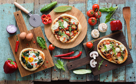 Flatlay of pizza party. Homemade pizzas and raw vegetables in abundance on oak chopping boards over shabby blue wooden background overhead viewの写真素材