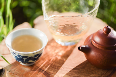 Healthy beverage. Green tea in Chinese clay teapot and cups on wood slab in morning light closeupの写真素材