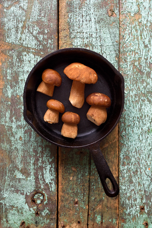 Wild forest mushrooms. Boletus edulis or porcini mushrooms in cast iron pan ready for frying on shabby blue background overhead viewの写真素材