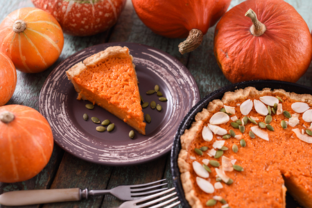 Homemade pumpkin pie with pumpkin seeds and almonds served with raw pumpkins closeupの写真素材