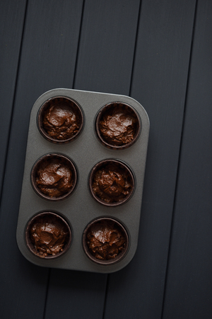 Minimalist style homemade pastry. Raw batter for chocolate muffins in metal baking tray on dark background top view copyspaceの写真素材