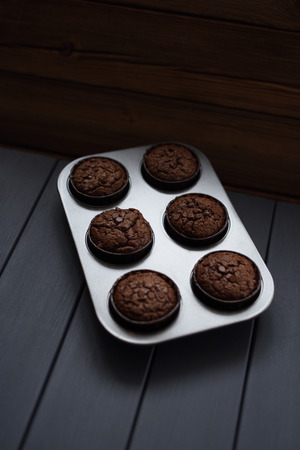 Minimalist style homemade pastry. Chocolate muffins with chocolate chips in metal baking tray on dark background copyspaceの写真素材