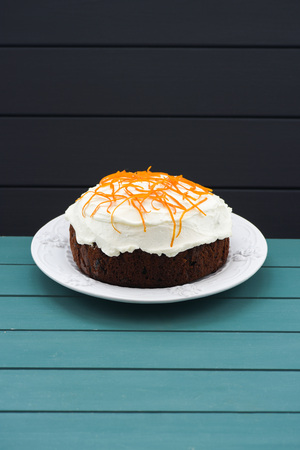 Minimalist style pastry. Homemade traditional fruit cake with cream icing and orange peel on blue...
