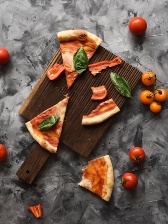 Messy table after pizza party. Remains of Italian pizza Margherita and raw tomatoes and bell pepper on dark background top viewの写真素材
