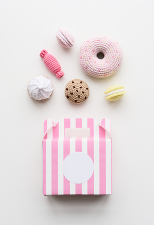 Flatlay of amigurumi toy sweets. Knitted cakes, candies and donuts with pink box on white background copy spaceの写真素材