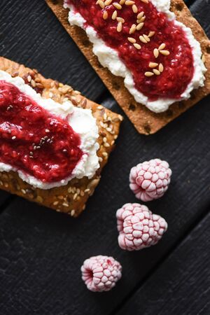 Healthy dessert flat lay. Chia seed jam with creamcheese, flax seeds and raspberries on wholegrain crispbread on black background copy spaceの写真素材