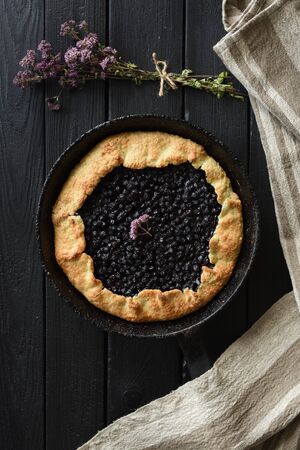 Homemade rustic pie. Blueberry galette in cast iron pan with linen cloth beside on dark background top viewの写真素材
