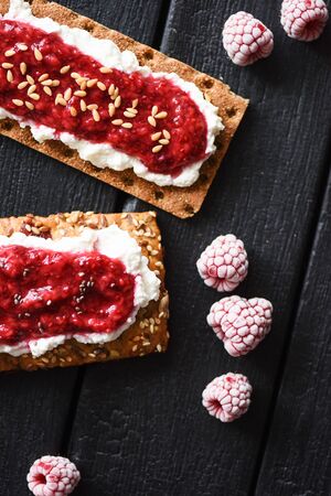 Healthy sugar free dessert. Raspberry chia jam and flax seeds on crispy bread and cream cheese with frozen berries on black background top viewの写真素材