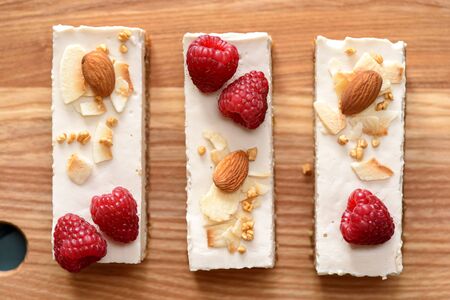 Vegan sweets. Coconut milk bars with raspberries, coconut flakes and almonds on wooden background top viewの写真素材