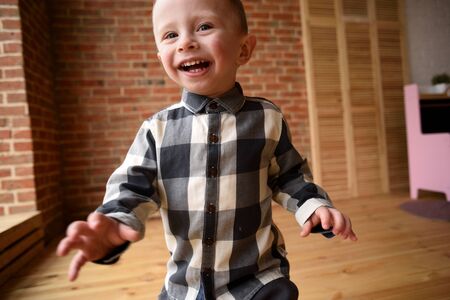 Happy child concept. Laughing toddler boy running in big empty room close up copy space