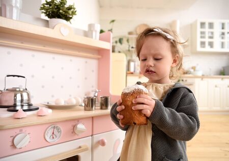 Kid eating sweets. Adorable toddler girl with Easter bread in light designer kitchen copy spaceの写真素材