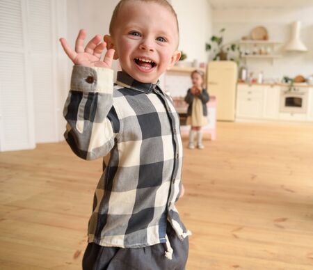 Children play concept. Cute toddler boy running laughing and blurred girl in play kitchen in spacious light room copy spaceの写真素材