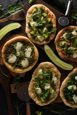 Green pizzas on dark background with cucumbers, vegetables, spinach and pizza cutter overhead viewの写真素材