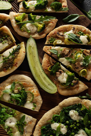 Green healthy pizzas cuts flat lay with cucumbers, paprika, mozzarella, spinach and pizza cutter overhead viewの写真素材