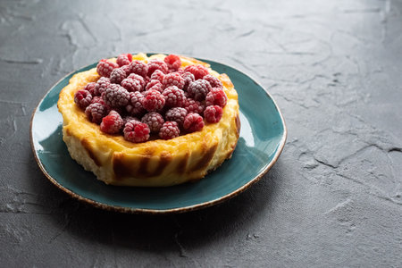 Raspberry homemade cheesecake on blue plate with dark plaster background closeupの写真素材