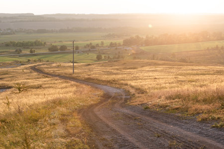 The bend of the village country road going down the hill, the rays of sunset landscapeの写真素材