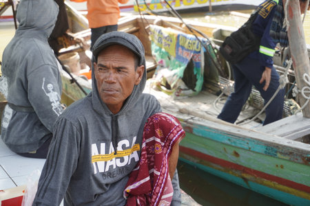 Surabaya, Indonesia - June 29, 2022 : fisherman in a hat sit near their boatのeditorial素材