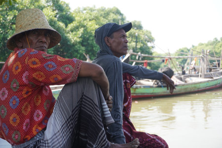 Surabaya, Indonesia - June 29, 2022 : fisherman in a hat sit near their boatのeditorial素材