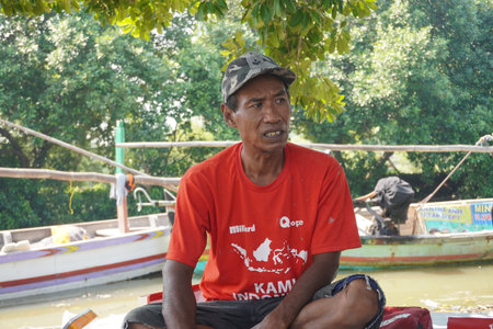 Surabaya, Indonesia - June 29, 2022 : fisherman in a hat sit near their boatのeditorial素材