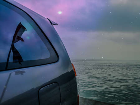 Car in the sea at night with starry sky and moon.