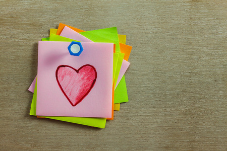red heart shape on colorful sticky note and peg on wood background.
