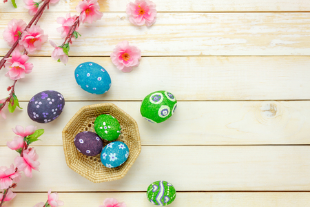 Top view easter background.Happy easter eggs pained on basket also beautiful pink flower.Texture rustic white wooden with decorations and copy space.の写真素材