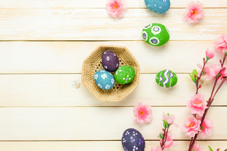 Top view easter background.Happy easter eggs pained on basket also beautiful pink flower.Texture rustic white wooden with decorations and copy space.の写真素材