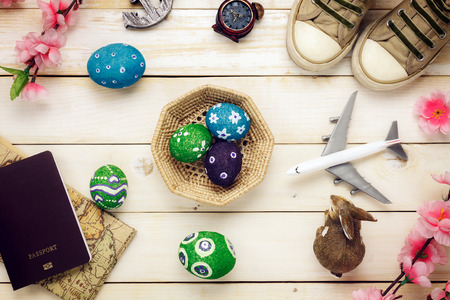 Top view Easter festival with holiday travel background.Happy easter eggs painted on basket also beautiful pink flower with rabbit doll and travel items.Texture rustic white wooden with decorations and copy space.の写真素材