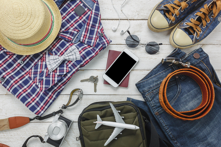 Top view accessoires to travel with man clothing concept. shirt,jean,mobile phone ,headphone on wooden background.passport,key,sunglasses and hat on wood table.の写真素材