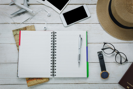 Top view accessoires to travel concept.Notebook free space for writing with pen on white table backgroun.Items is map,watch,eyeglasses,passport,hat,mobilephone,airplane,eyephone,photo.の写真素材