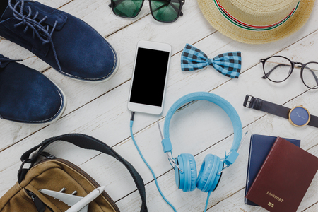Top view accessoires to travel concept.mobile phone listening music by headphone on wooden background.Man'shoes,airplane,bag,passport,bow tie,watch,sunglasses on white wood table.flat lay.copy space.の写真素材