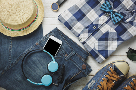 Top view accessoires to travel with man clothing concept.the essential shirt,jean,mobile phone ,headphone on white wooden background.passport,key,sunglasses and hat on wood table.flat lay.copy space.の写真素材