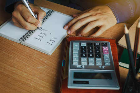 hand Asian man calculate finances and accounting for monthly expenses / charges or cost on notebook with accessories in home office room.Idea to save / security money and control income or recipe.の写真素材