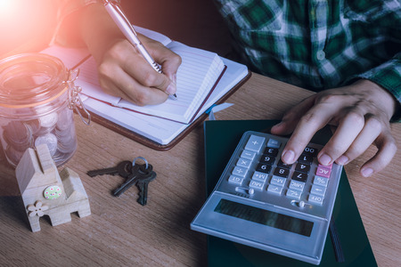 Asian man accountant or banker calculate finances / savings money or economy for rent home / house or condominium.Idea for save coin.Essential accessories on table office desk.Sun flare light.の写真素材