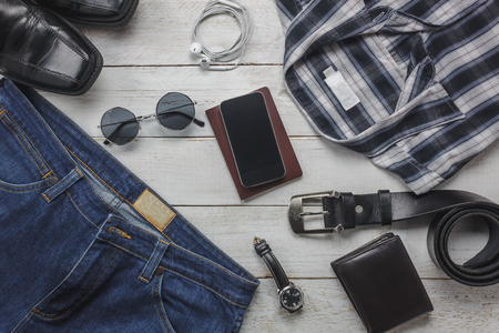 Top view / Flat lay accessory to travel with man / gentlemen clothing concept.Items the shirt jean and mobile phone on rustic white wooden background.watch,sunglasses and shoes on wood table .の写真素材