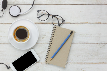 Top view / Flat Lay the pencil / note book / white mobile phone / listening radio music by headphones / black coffee and eyeglasses on rustic table wooden.An idea to relax time / rest or take a break.の写真素材