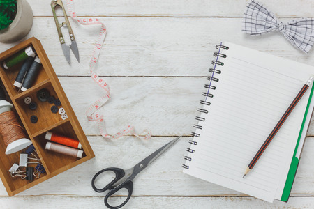 Top view accessories tailor concept.Tailor tools is cutting scissors,bow tie, spools of thread, buttons and sewing clothes. Notebook for free space text on rustic wooden background.の写真素材