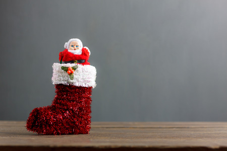Santa claus doll stand in red sock festive ornaments Merry Christmas concept.Blur grey background with copy space area.Essential items & sign decorations on modern rustic wooden at home office desk.の写真素材