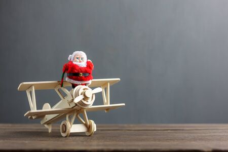 Festive decoration Merry Christmas & Happy new year concept background.Santa claus doll on vintage airplane toy ready to travel.Essential accessories on the modern rustic wood and blur grey backdrop.の写真素材