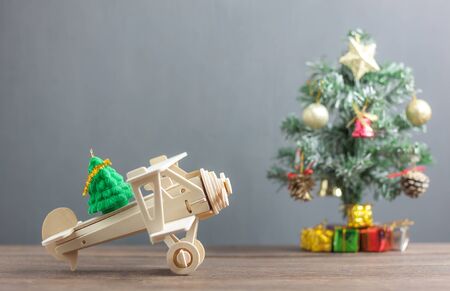 Toy wood airplane transfer fir tree with Blur Christmas tree & many beautiful gift box also essential decoration accessory.Variety objects on modern rustic brown wooden plank and blur grey background.の写真素材