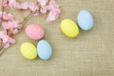 Table top view shot of arrangement decoration Happy Easter holiday background concept.Flat lay colorful bunny egg with pink blossom on brown sackcloth at home office desk.Space for creative design.の写真素材
