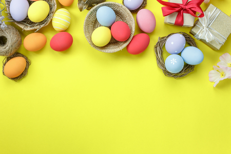 Table top view shot of arrangement decoration Happy Easter holiday background concept.Flat lay colorful bunny eggs with pink blossom on yellow paper at home office desk.Space for creative design.の写真素材